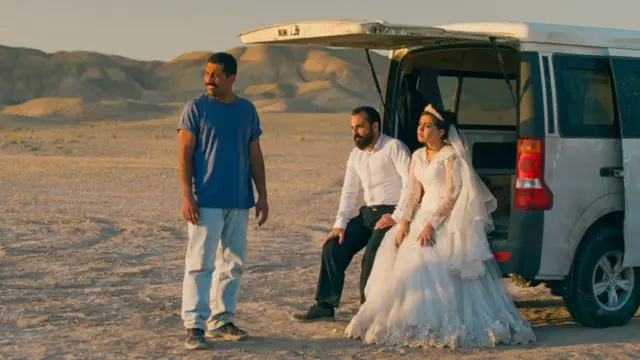 Una novia y un novio sentados en la parte trasera de una van y otro hombre de pie junto a ellos en el desierto iraní en una imagen de It Was Just an Accident.