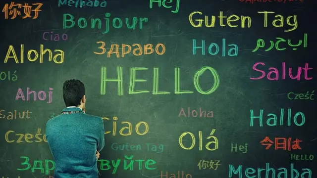 Hombre de espaldas frente a un pizarrón en el que hay escritos saludos en diferentes idiomas