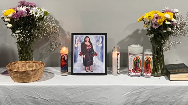 Una mesa en la que se ve la foto de la fallecida, María Florinda Ríos Pérez, junto a velas y floreros con flores.