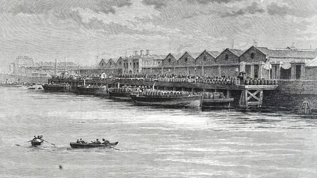 Un grabado antiguo muestra un puerto con almacenes y barcos cargados de barriles en la orilla, mientras pequeñas embarcaciones navegan en el río.