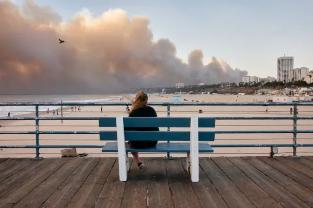 Mujer observa desde un banco del muelle de Santa Mónica el incendio en Pacific Palisades, Los Ángeles, California, Estados Unidos, el 7 de enero de 2025. (Marcus Ubungen / Los Angeles Times via Getty Images)