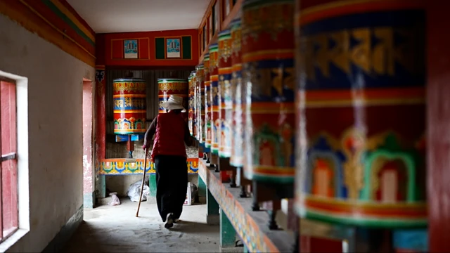 Una mujer pasa junto a coloridos molinos de oración que representan murales de la vida de Buda dentro del monasterio de Kirti.