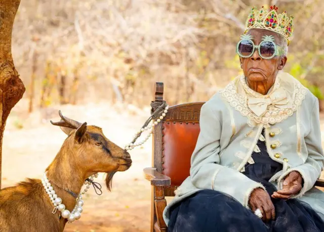 Margret Chola con una corona junto a una cabra que lleva un collar de perlas