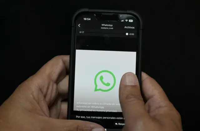 Una persona sostiene su teléfono y se ve el logo de WhatsApp.