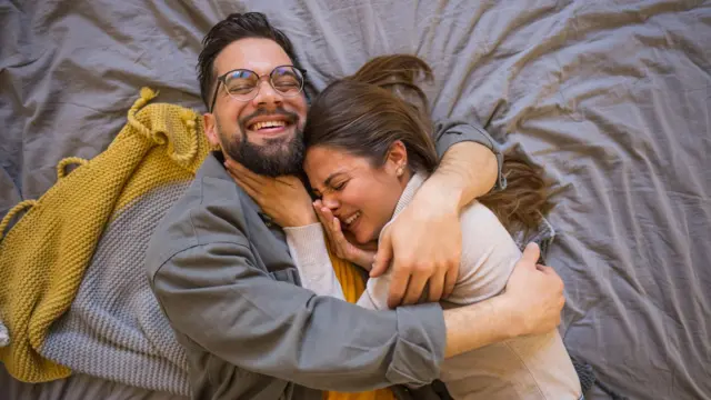 Una pareja abrazada sobre una cama. 