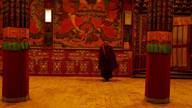 Un monje dentro de un monasterio cuyas paredes están cubiertas de murales en intensos tonos rojos.
