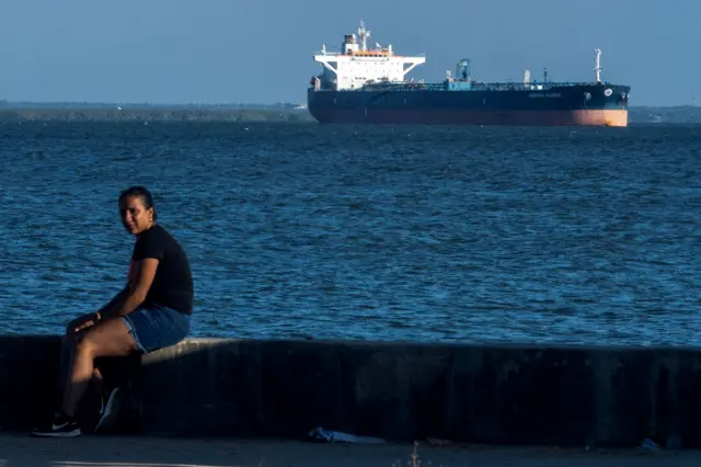 Una mujer sentada en el malecón del lago de Maracaibo y a lo lejos un tanquero de petrolero.