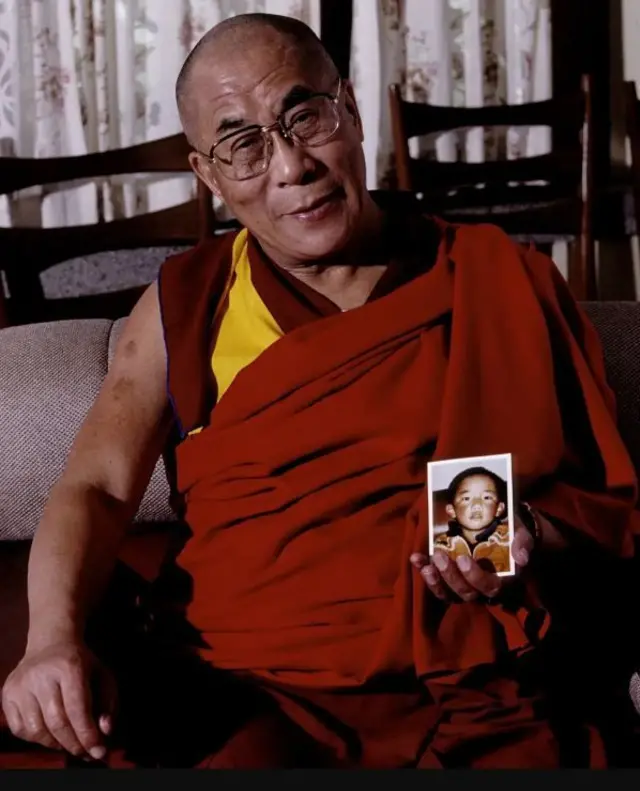 El Dalai Lama, con su característica túnica roja y amarilla, sostiene en su mano izquierda la única fotografía conocida del Panchen Lama.