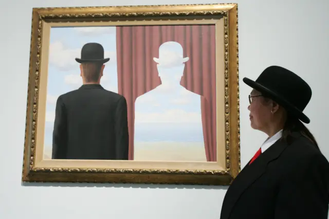 Mujer con sombrero frente a cuadro de Magritte que muestra a un hombre con sombrero al lado de una cortina en la que su silueta está recortada