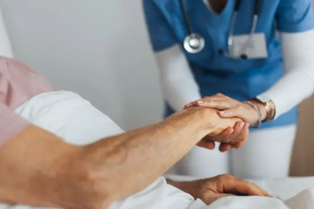 Una enfermera sostiene la mano de un enfermo