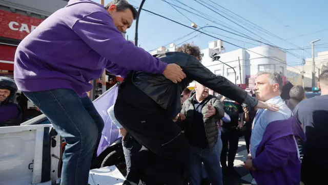 Milei es evacuado del mitin en la provincia de buenos aires donde le lanzaron piedras. Se ve cómo su seguridad lo ayuda a bajarse de una camioneta blanca.
