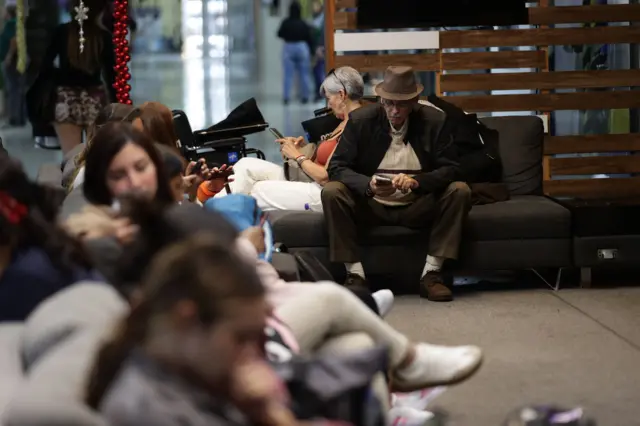 Pasajeros en el aeropuerto de Maiquetía sentados aguardando por información de su vuelo.