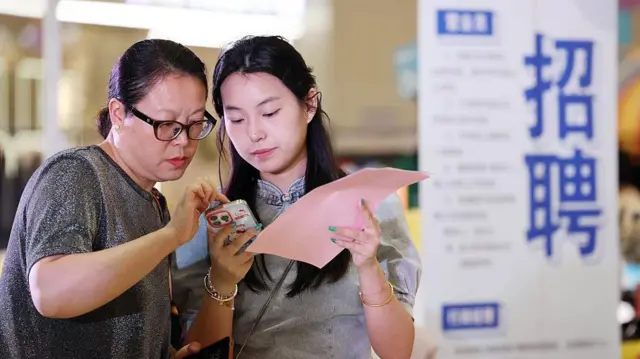 Dos mujeres miran las instrucciones de un teléfono en una feria de empleo en la ciudad china de Lianyungang. 