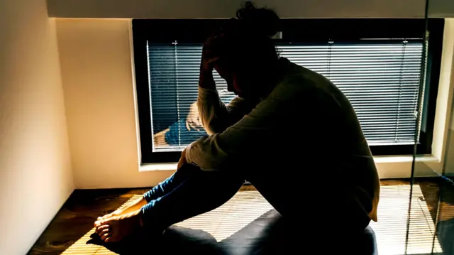 Una silueta de una mujer sentada frente a una pequeña ventana.