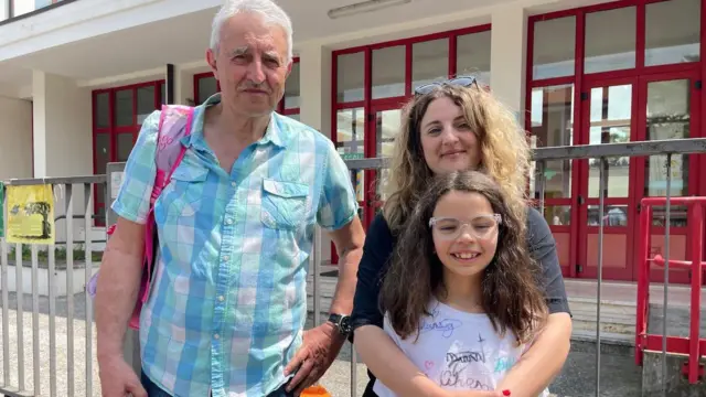 Un hombre mayor, una madre y su hija frente a un edificio   
