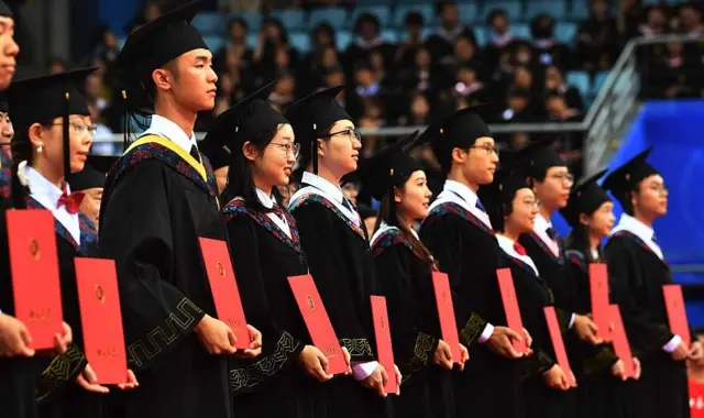 Jóvenes con togas muestran sus diplomas durante su ceremonia de graduación en la Universidad de Pekín
