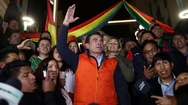Rodrigo Paz con chaleco rojo yrodeado de partidarios levanta el brazo derecho