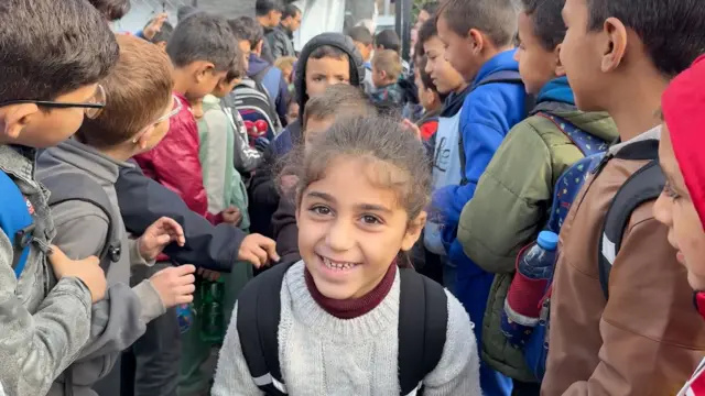 Una niña sonriente rodeada de otros niños en la puerta de una escuela en Gaza.