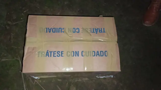 La caja de cartón cerrada con cinta y con un mensaje en azul que dice 