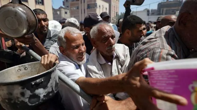 Un grupo de hombres agolpados sujetan recipientes a la espera de recibir ayuda humanitaria en Gaza.