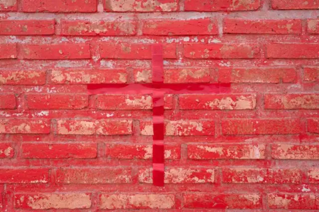 Un muro de ladrillo pintado de rojo con una cinta roja pegada en forma de cruz