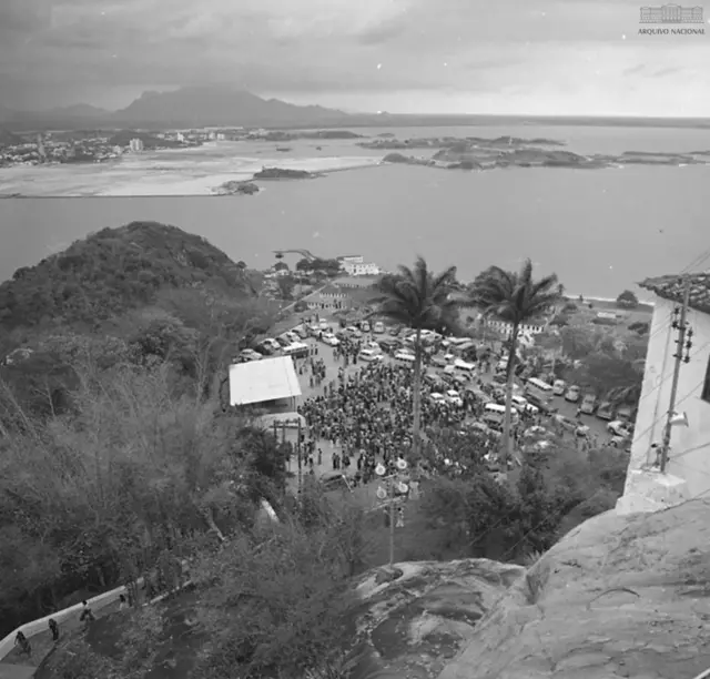 Foto en blanco y negro de la vista desde lo alto de una piedra que muestra el mar y una ciudad en el fondo