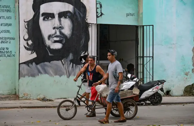 Dos personas empujan un triciclo bajo un retrato del 