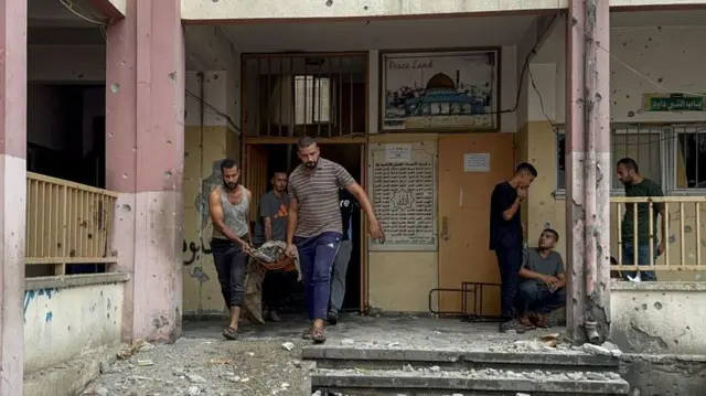 Varios hombres sacan un cadáver de un colegio bombardeado.