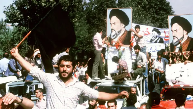 Un manifestante en una camisa de cuadros claros ondea una bandera negra mientras otros portan fotos del ayatolá Jomeini, el exiliado líder religioso, el 8 de septiembre de 1978, en protesta contra el sha en las calles de Teherán  