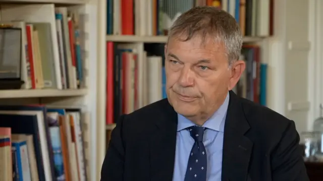 Philippe Lazzarini está sentado frente a una estantería blanca.