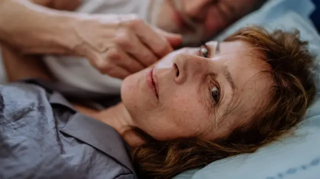 Una mujer mayor siendo acariciada en el rostro por un hombre. 