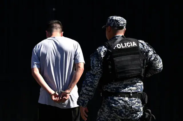 Un hombre arrestado por supuestos vínculos con pandillas es escoltado por un oficial de la Policía Nacional Civil durante el estado de emergencia declarado por el gobierno salvadoreño en el centro penal de San Salvador, el 22 de junio de 2022. (Foto de MARVIN RECINOS / AFP) (Foto de MARVIN RECINOS/AFP a través de Getty Images)