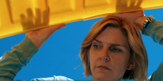 Una mujer sujeta lo que parece ser la tapadera de un contenedor y mira en su interior. 