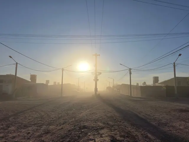 Calle de tierra, nube de polvo y el sol del amanecer.