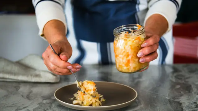 Una mano coloca con una cuchara comida fermentada en un plato.