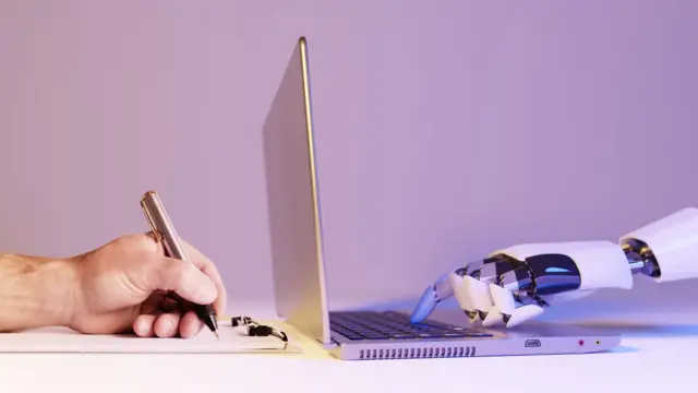 Una mano sostiene un bolígrafo y escribe en un papel y al otro lado una mano robótica pulsa una tecla en una computadora portátil