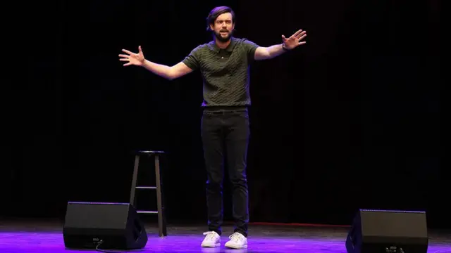 Una foto de Jack Whitehall en un escenario mientras presenta su monólogo.