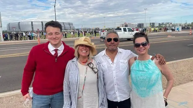Un grupo de cuatro personas, dos hombres y dos mujeres, sonríen a cámara, mientras en el fondo se divisa un estadio y una larga fila  de personas esperando entrar