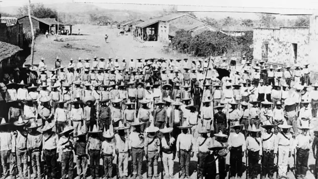 Filas de hombres con sus rifles en un pueblo