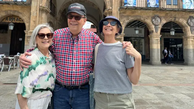 Carlos Montaner abrazado a su esposa, Linda, y su hija, GIna. Los tres sonríen en una plaza.