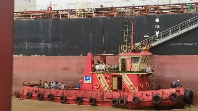 Los tripulantes del buque Nirvana fueron repatriados tras pasar meses en el mar, pero siguen esperando el pago de sus salarios. Se les ve de pie en una embarcación junto a su buque, a la espera de ser repatriados a tierra.