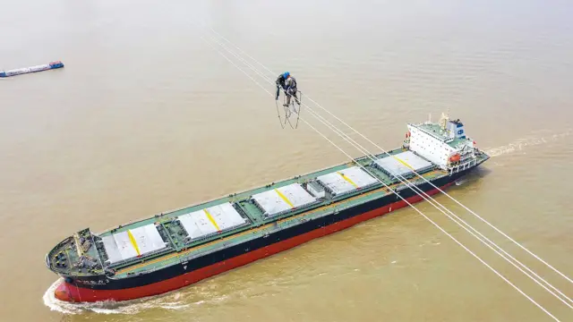 Dos trabajadores sobre líneas UHV mientras pasa un barco debajo