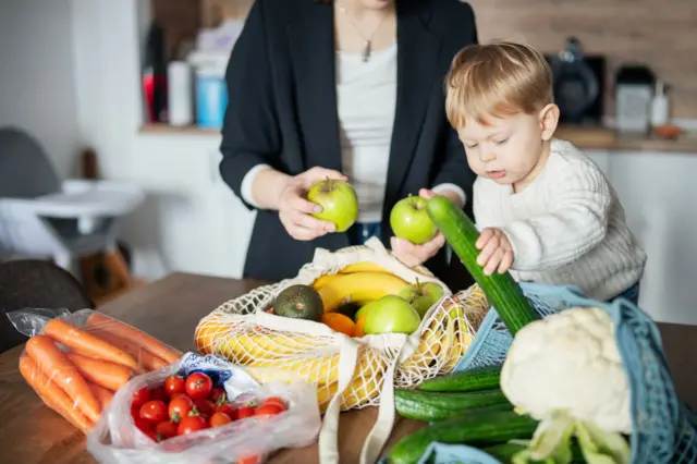 Una mamá tiene un bebé en una mesa y está jugando con vegetales