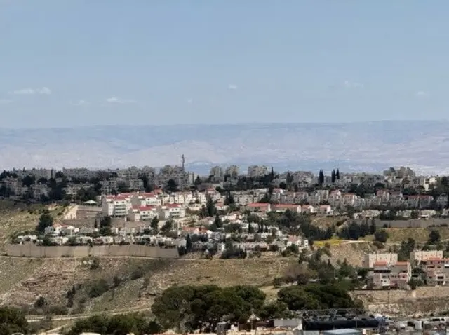 En la foto tomada durante el día se ven los edificios de la colonia de Maale Adumim, construida en una colina y rodeada de árboles.