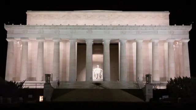 El Monumento a Lincoln iluminado por la noche. Se puede ver una gran estatua del expresidente estadounidense Abraham Lincoln iluminada entre las columnas del gran edificio en el que se encuentra la estatua.