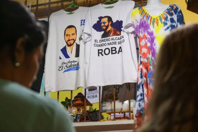 Dos mujeres delante de camisetas con imágenes y frases de Bukele en El Salvador