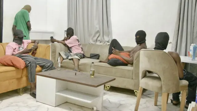 Cuatro jóvenes encapuchados sentados en sofás y sillas con teléfonos en sus manos