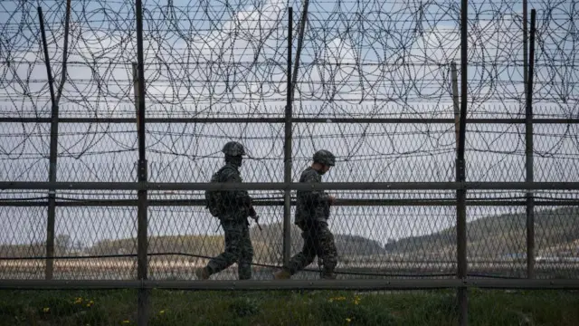 La cerca de alambre de púas con dos guardias que patrullan el área.