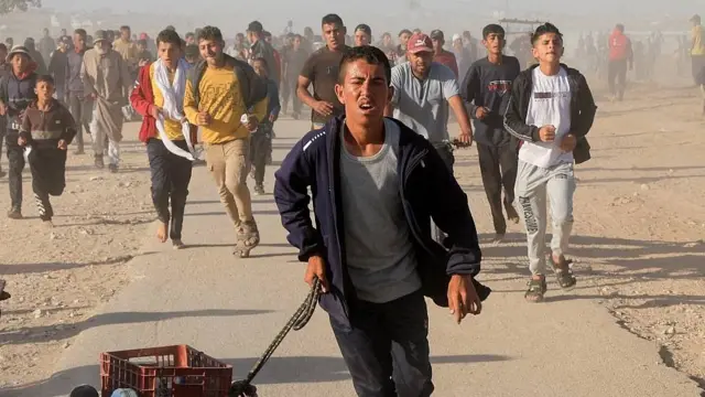 Jóvenes palestinos corriendo a uno de los puntos de distribución de la Fundación Humanitaria de Gaza con la esperanza de recibir raciones