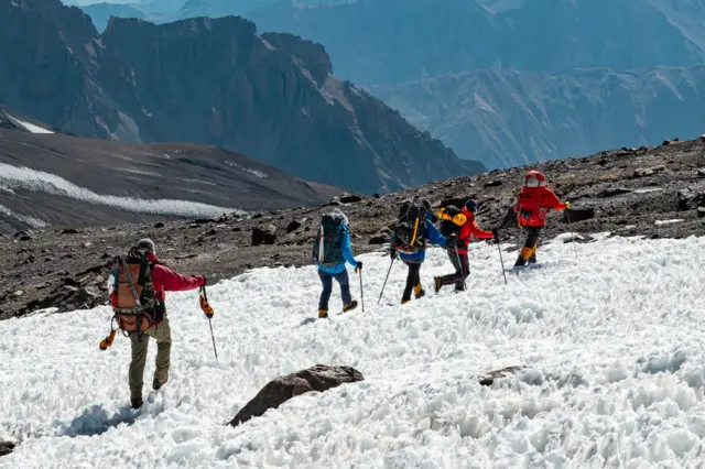 Cinco personas, ataviadas con ropa de abrigo de montaña, caminando entre la nieve.